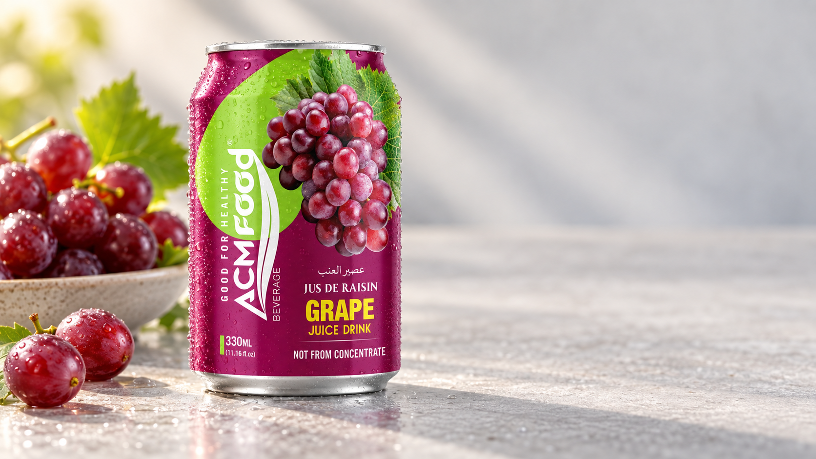 Close-up of a finished bottled fruit beverage on a clean light grey surface, condensation on the glass, a shallow dish of fresh fruit slightly out of focus behind it, warm natural side light, generous negative space to the right, realistic commercial product photography, landscape composition, unbranded packaging