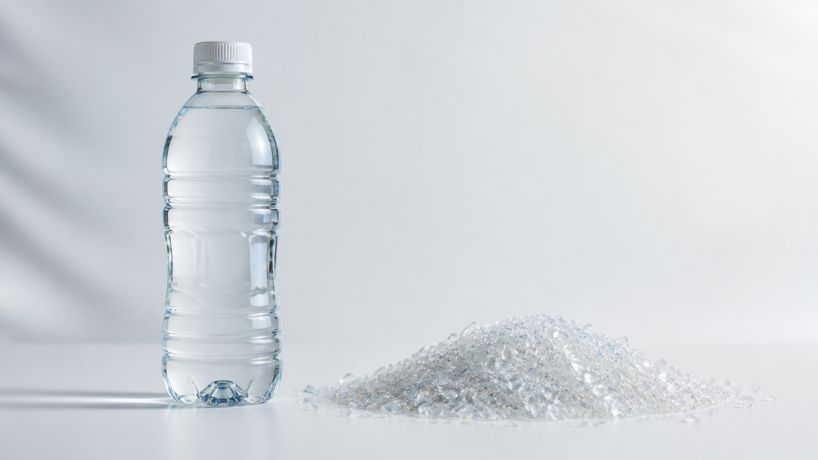 Clear rPET beverage bottle beside clean PET flakes on white background